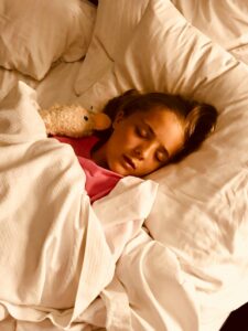 Young girl sleeping peacefully with stuffed animal in a cozy white bed.